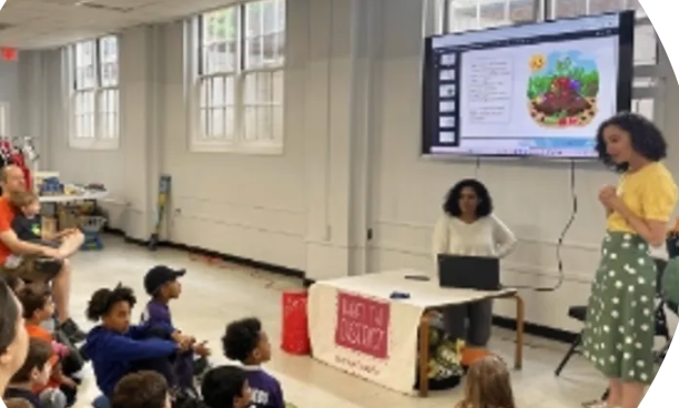 Stephanie next to a TV in a classroom with children sitting on the floor